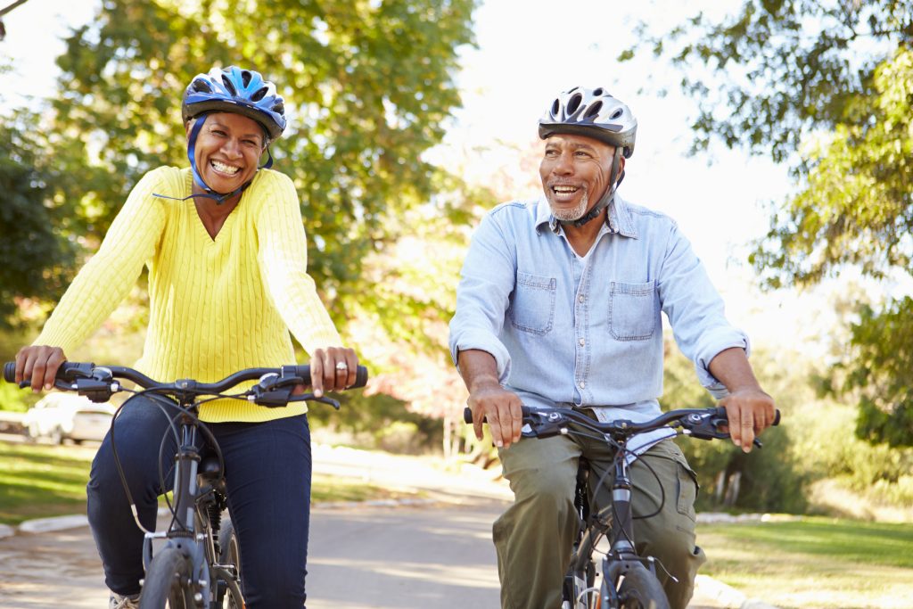 Deux seniors souriant et portant des casques en faisant du vélo sur un chemin.