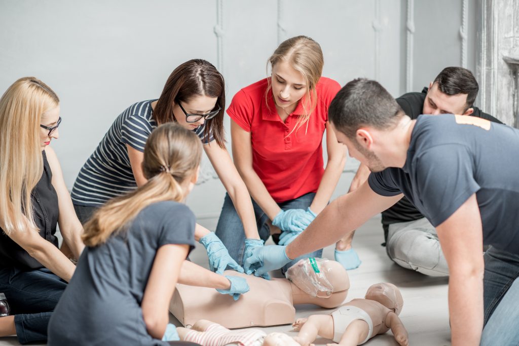 Group of people learning how to make first aid heart compressions with dummies
