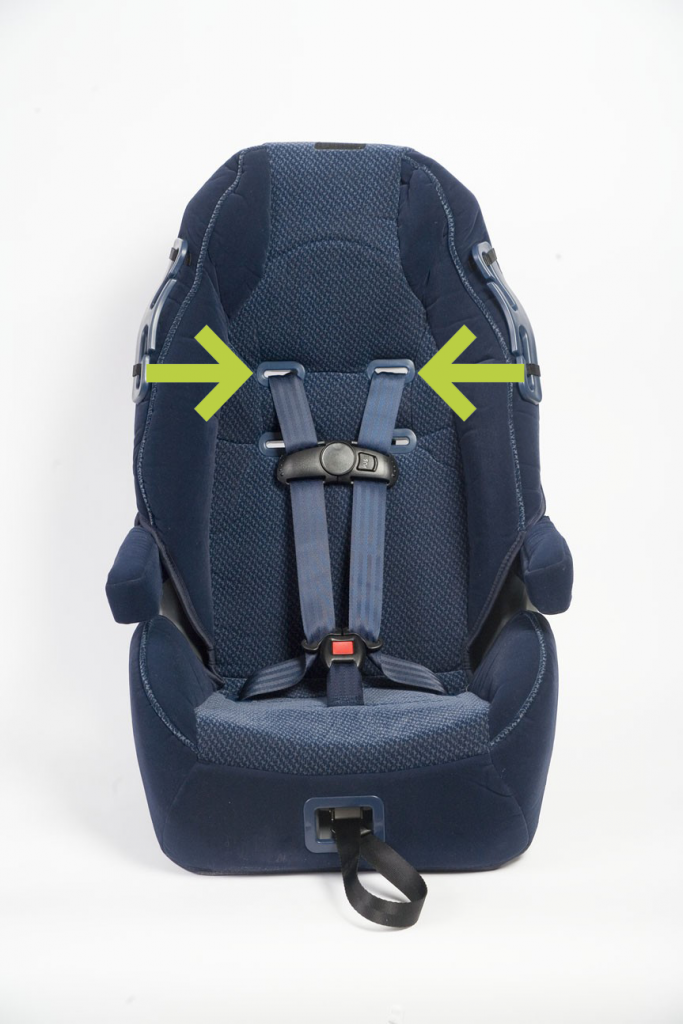 Green arrows point to the harness slots on the frame of a car seat
